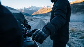 Beheizbare Motorradhandschuhe am Lenker auf einer frostigen Alpenstraße bei Sonnenaufgang